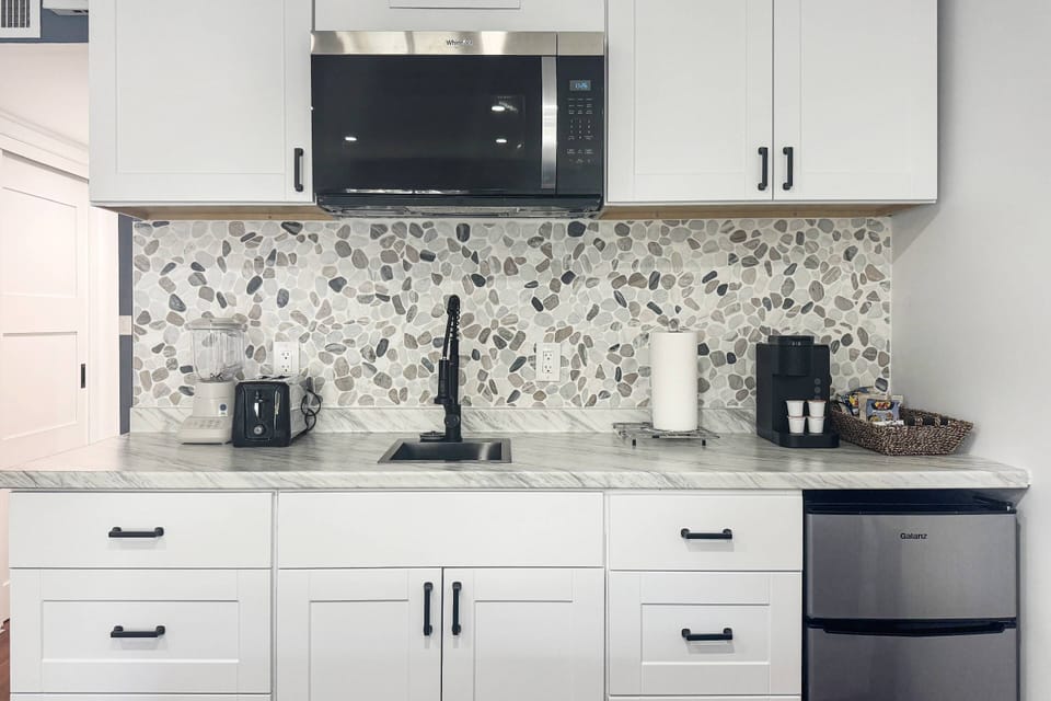 Contemporary kitchenette with appliances, coffee station, and stylish pebble-tile backsplash.