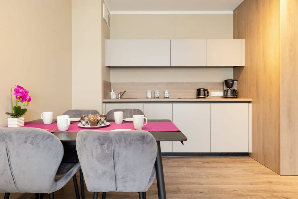 A fully equipped modern kitchenette with white cabinetry, alongside a dining table with upholstered chairs.