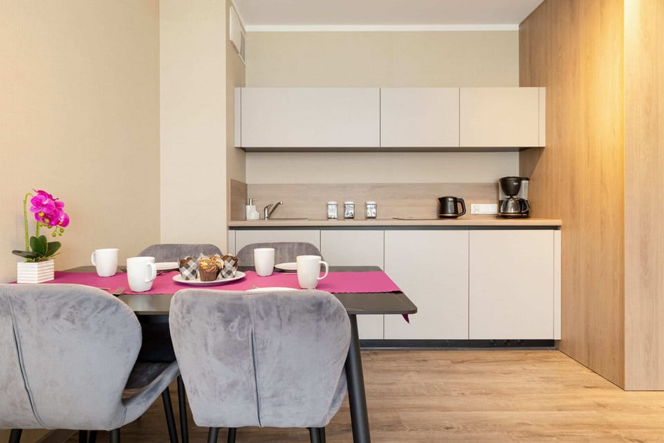 A fully equipped modern kitchenette with white cabinetry, alongside a dining table with upholstered chairs.