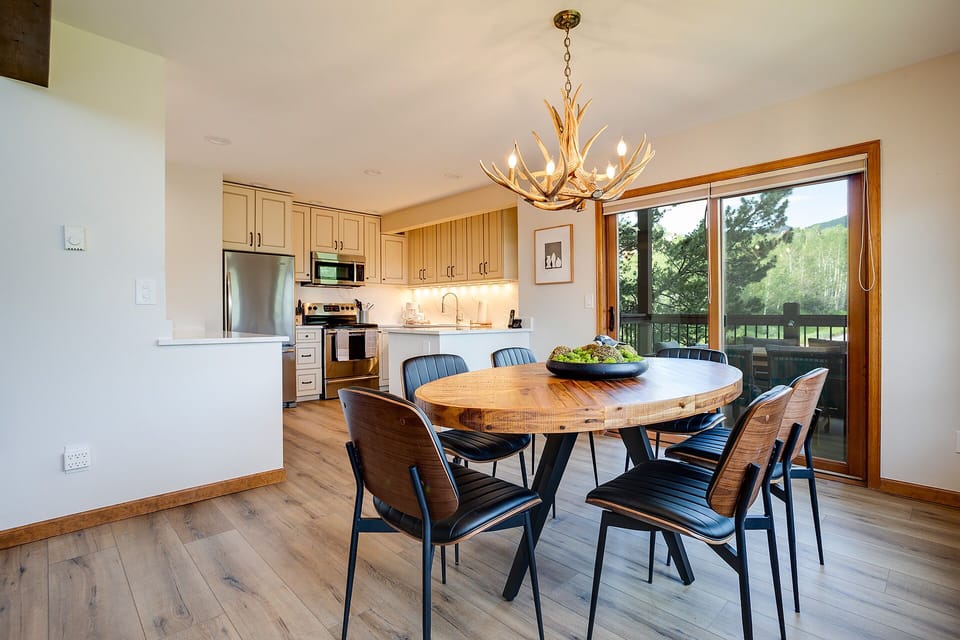 Gather around your beautiful dining table under rustic antler lighting, with your fully-equipped kitchen steps away and serene mountain views beyond.