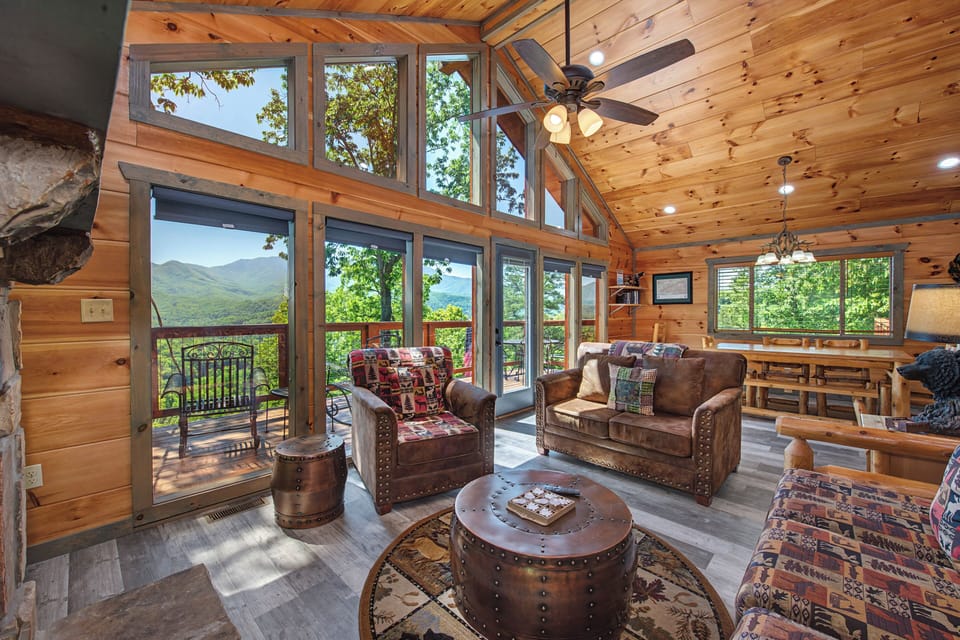 Relax in your sunlit living room with soaring ceilings and floor-to-ceiling windows framing breathtaking mountain views. Cozy leather seating invites you to unwind and savor the scenery from your private deck.