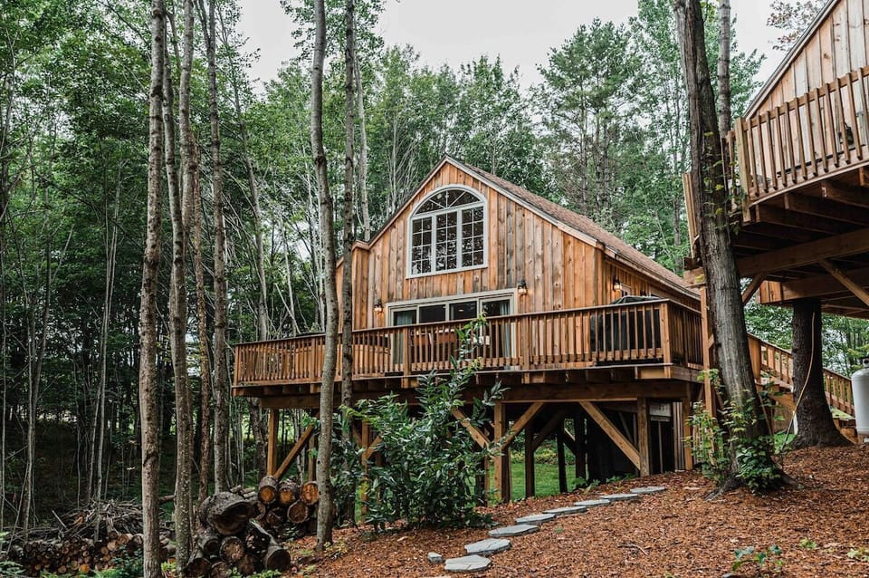 The exterior of the MoonLight Treehouse is surrounded by lush greenery, with a large front deck perfect for relaxing. The stunning woodwork and architectural details create a cozy, secluded atmosphere among the trees.
