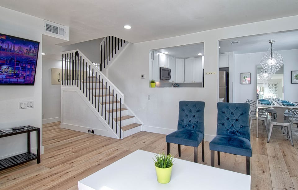 - Bright open living area with cozy seating and clean design layout   - White walls and natural wood flooring create a warm atmosphere   - Spacious spot to relax with direct access to the kitchen area
