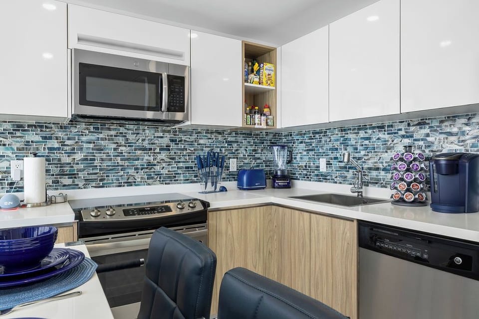 Your modern kitchen is ready for everything from morning coffee to home-cooked meals, with sleek counters, stainless appliances, and a stylish blue tile backsplash adding coastal charm.