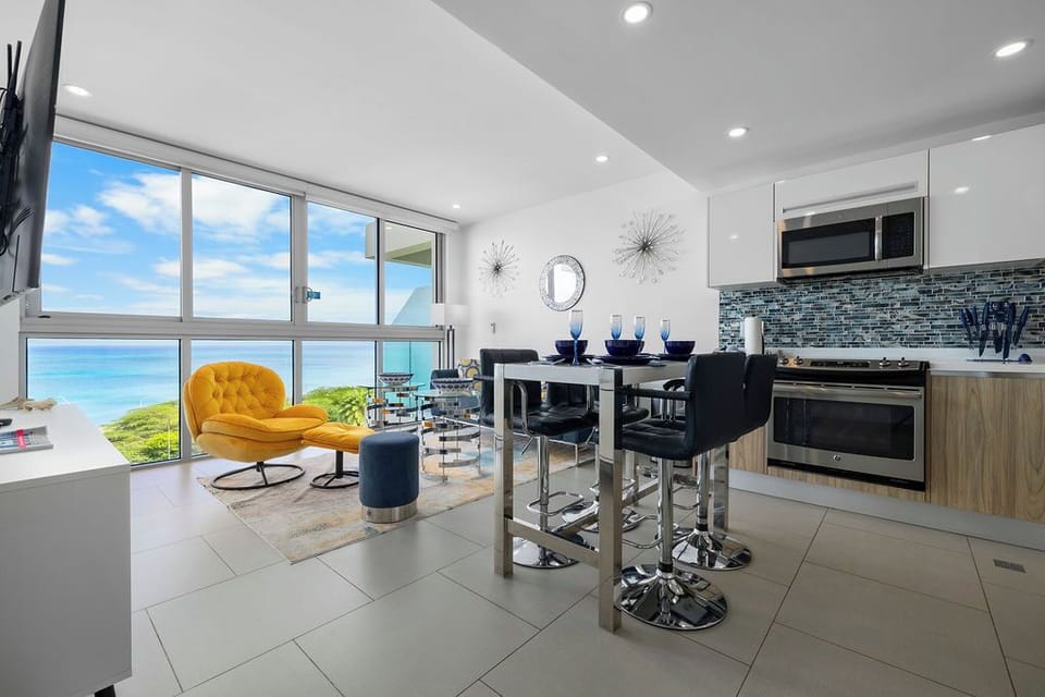 Stunning oceanfront views frame your modern open-concept living space, where a sleek kitchen, chic dining area, and cozy seating invite you to relax in contemporary beachside luxury.