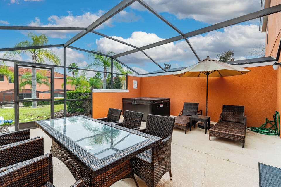 Enjoy al fresco dining on the charming screened patio with a glass-top table and wicker chairs. Relax on comfortable loungers and take in the vibrant orange walls that create an inviting atmosphere for your experience.