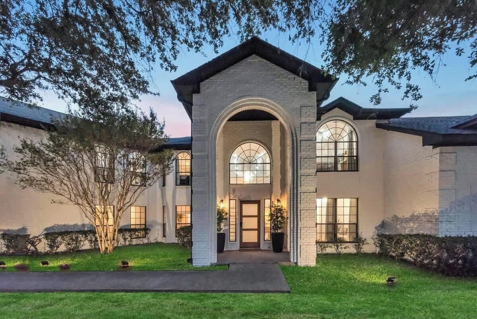 A grand lakefront home with a stunning entrance, beautifully lit in the evening to welcome you to a memorable stay.