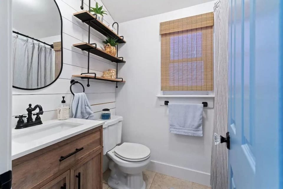 This newly renovated bathroom features a modern farmhouse style with a wood vanity, open shelving, and shiplap walls.