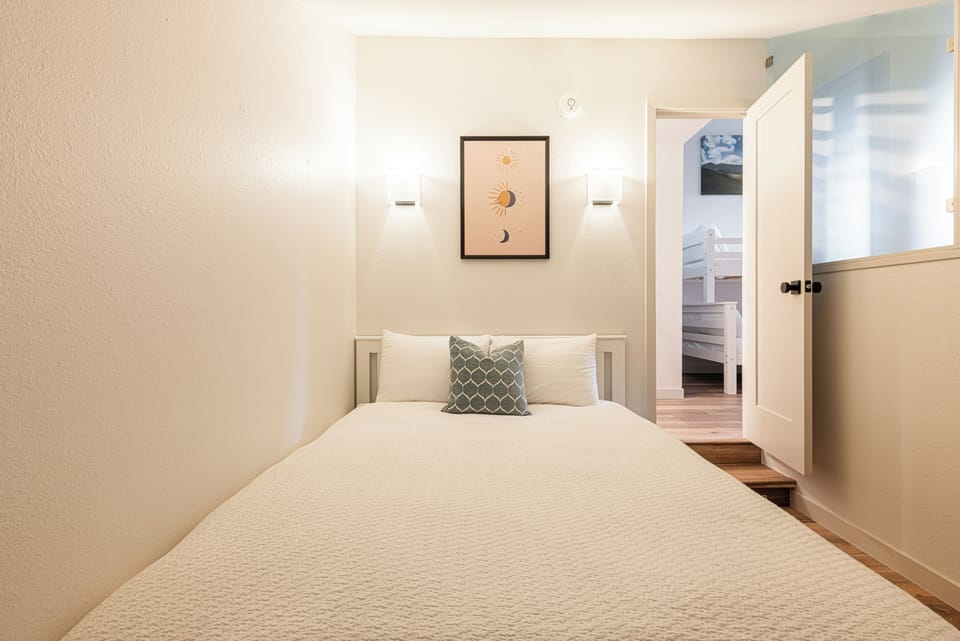 Bright queen bedroom with large windows and soft, inviting bedding.