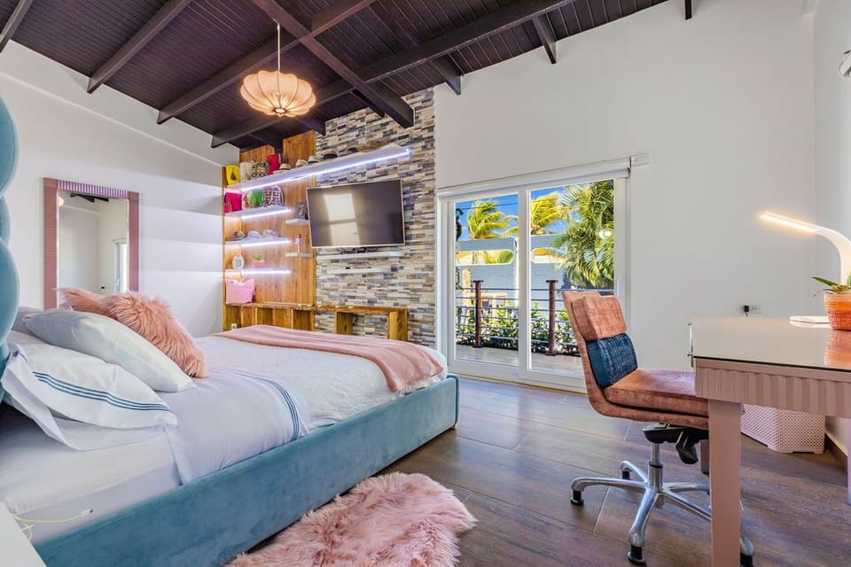 This bedroom features a feminine interior design. With an air-conditioning unit, a desk, TV, a balcony, a king bed, and a gorgeous bedframe.