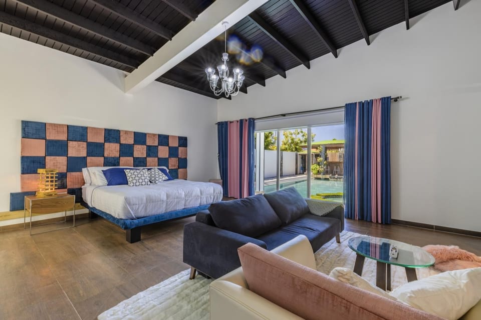 The master bedroom features 1 king bed and a sofa bed. Decorated with an elegant chandelier, large television, and  a large sliding door with a view of a beautiful garden.