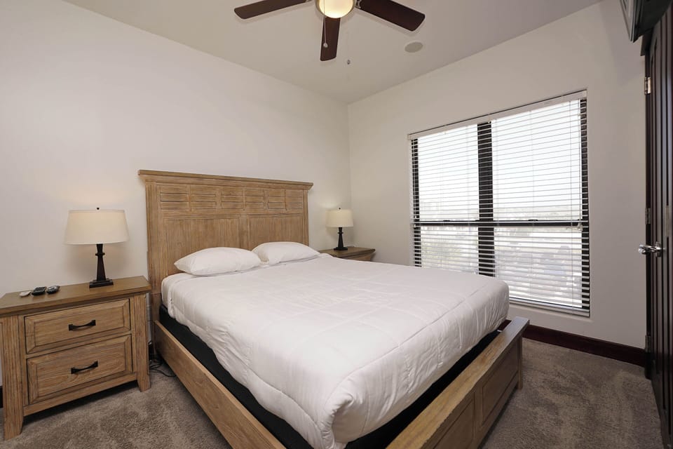 Your peaceful bedroom features a comfortable bed with crisp linens, warm wood furnishings, and gentle ceiling fan for perfect sleep comfort.