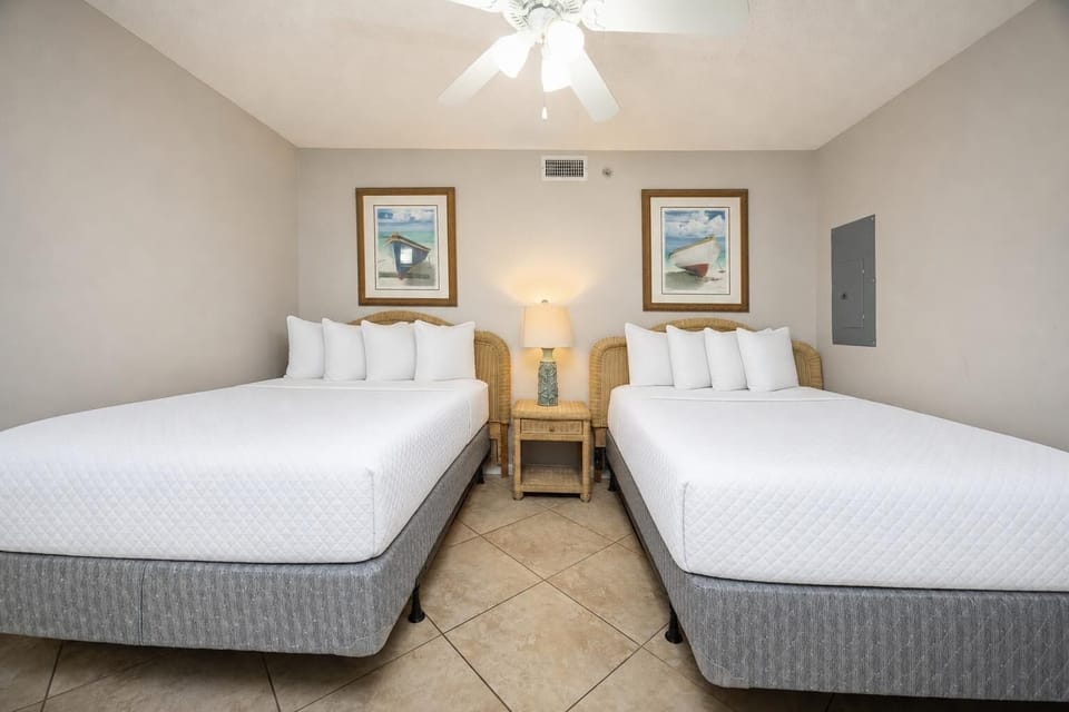 Two double beds with plush white bedding and coastal artwork create a serene atmosphere in this inviting guest bedroom