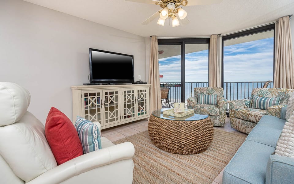Cozy living area features a light blue sofa with queen sleeper, tropical-patterned chairs, and a view of the gulf