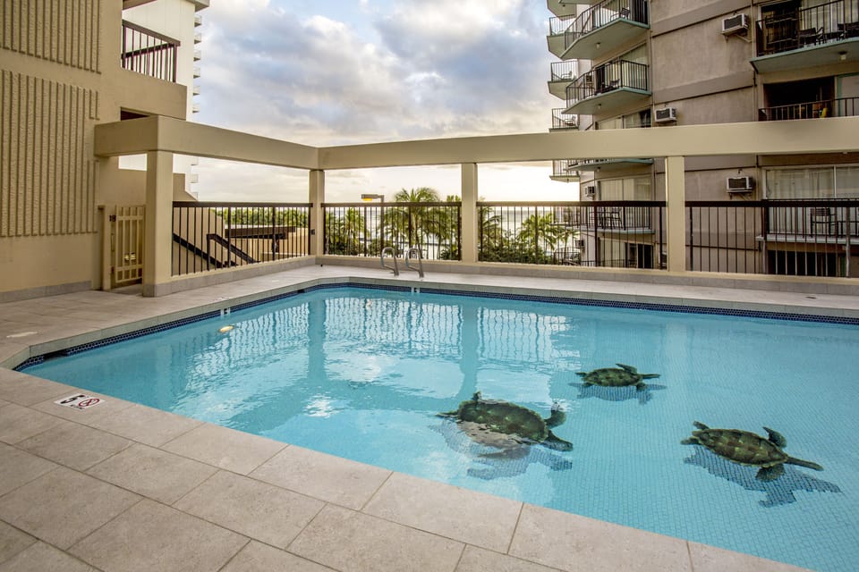 A serene outdoor pool features charming turtle tile art on the floor, inviting you to relax under the open sky surrounded by tropical greenery and modern architecture.