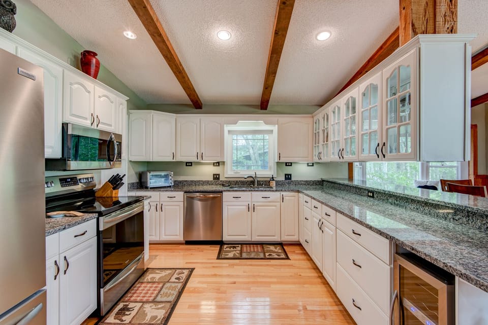 A fully equipped kitchen ready for mountain meals, with granite counters, stainless appliances, and warm wood beams overhead.