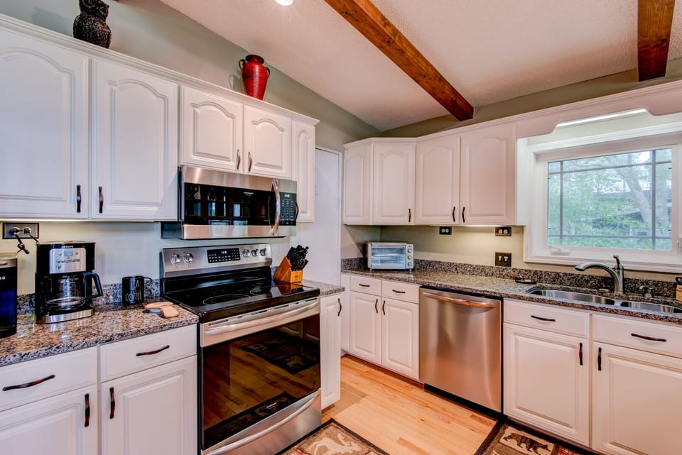 A fully equipped kitchen ready for mountain mornings, with granite counters, stainless appliances, and warm wood beams overhead.