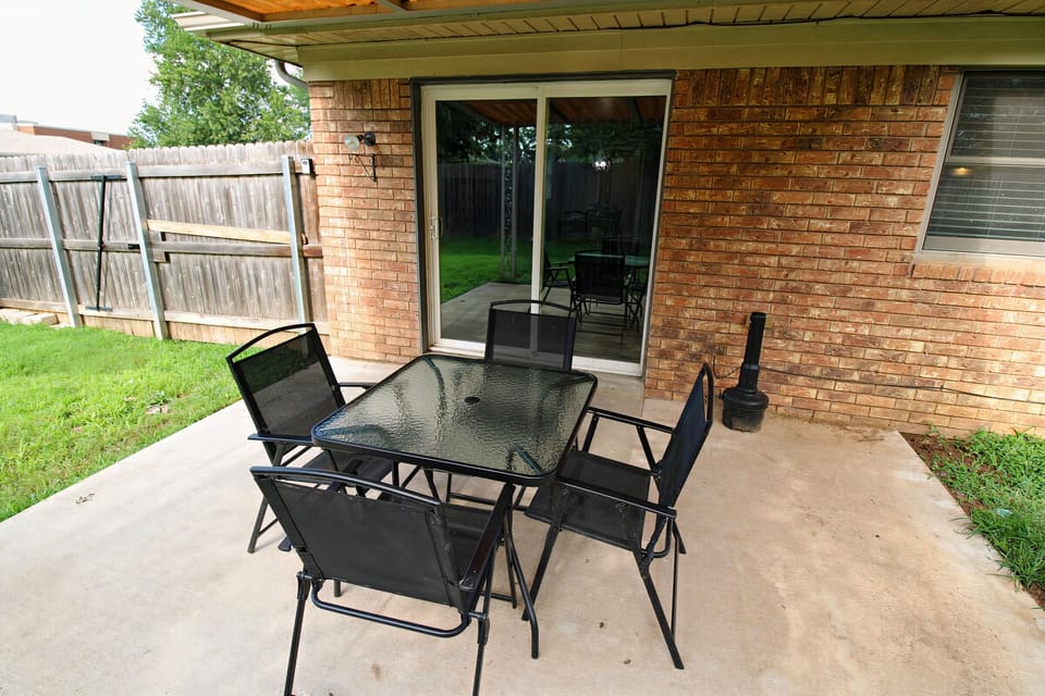 Backyard has charcoal grill, covered patio with furniture, fully fenced yard