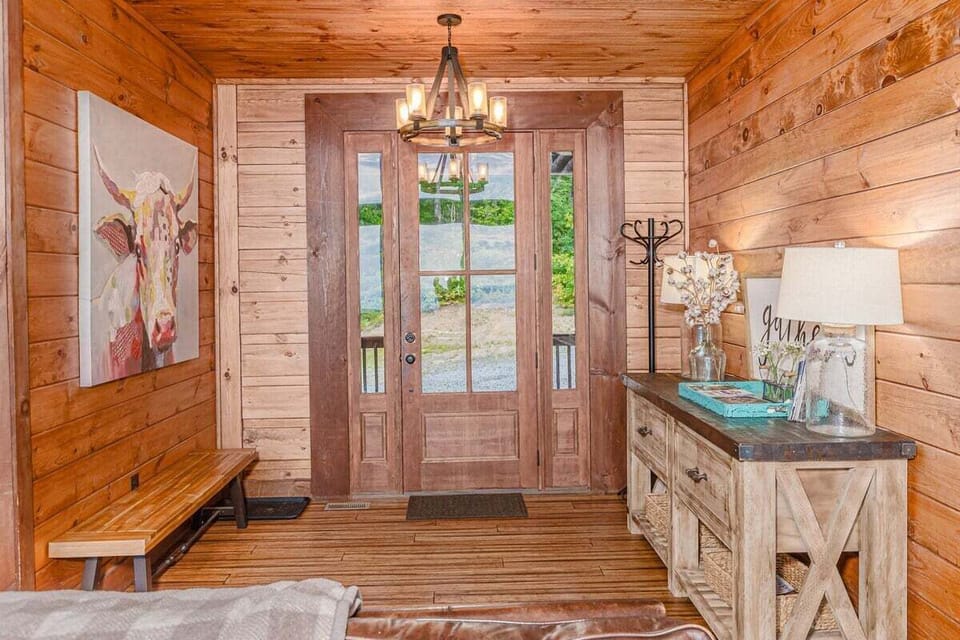 Rustic cabin entry with double wood front doors, bench seating, console table, and decorative lighting. Bright welcoming entrance at Sequoyah Sunset in Bryson City near the Great Smoky Mountains.