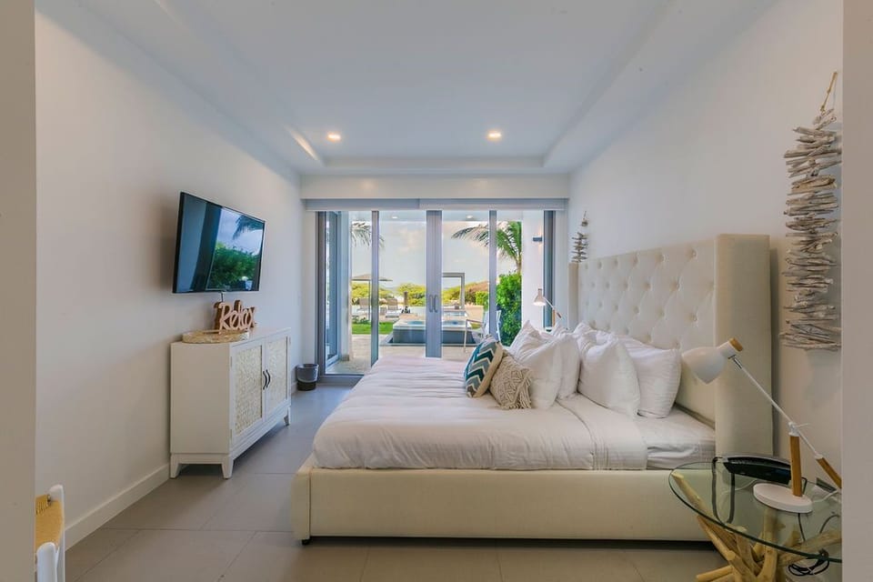 Picture yourself unwinding on this plush bed with crisp linens, while tropical views and your private pool await just beyond the glass doors—pure relaxation awaits.