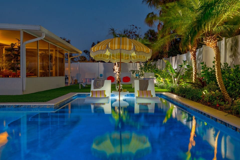 Private pool lit up at night with palms, ambient lighting, and a relaxed retro-coastal vibe.