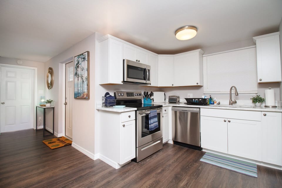 Modern kitchen with upgraded appliances like a 2-door stainless steel fridge, stove, oven, coffee maker, dishwasher, basic cooking utensils, dishware, silverware, glasses, toaster, and microwave.