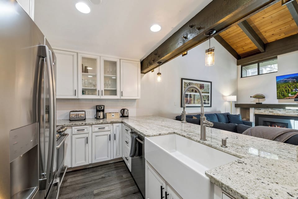 Your modern kitchen boasts granite countertops, stainless steel appliances, and a farmhouse sink—perfect for preparing meals during your mountain getaway. The open design flows into the cozy living space, creating an inviting atmosphere.
