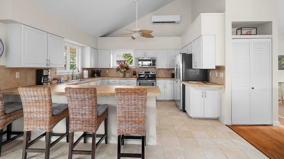 Gather around the spacious kitchen island with seating for three, featuring modern appliances, ample cabinet storage, and tropical ceiling fan—perfect for preparing meals and sharing stories together.