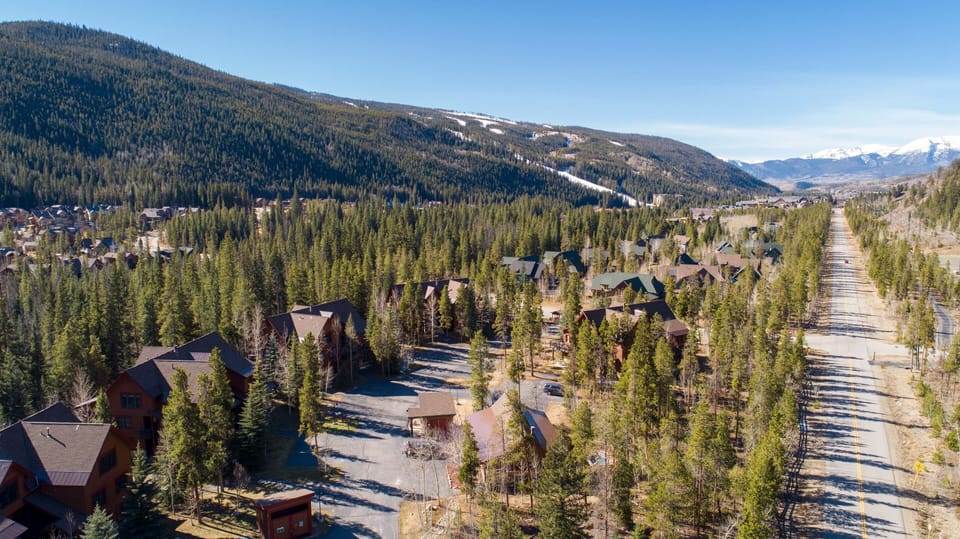Aerial view of a forested mountainous area with scattered houses and a long, straight road running through the valley on a clear day.
