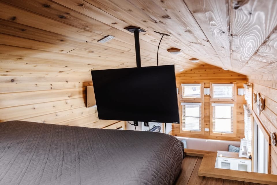 Queen bed in the tiny home’s open loft, featuring warm wood finishes and a TV for relaxing after a day of adventure near Zion National Park.