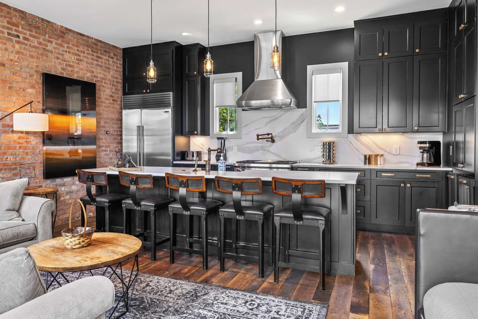 Spacious and inviting living room featuring comfortable sectional seating, exposed brick walls, a Smart TV, and an open-concept layout that flows seamlessly into the kitchen and dining area.
