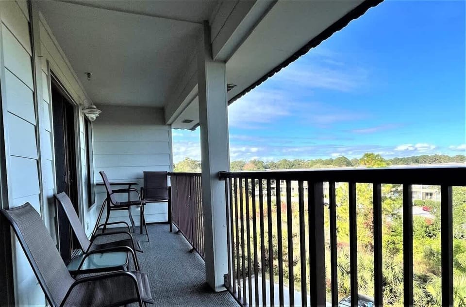 A long, shaded balcony equipped with comfortable lounge chairs and a small table. 