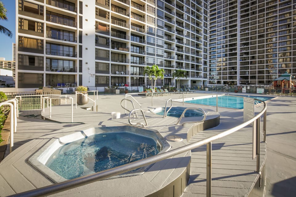 A spacious resort-style pool deck with hot tubs and lounging areas, set against a modern residential tower—your perfect spot to unwind under the sun.