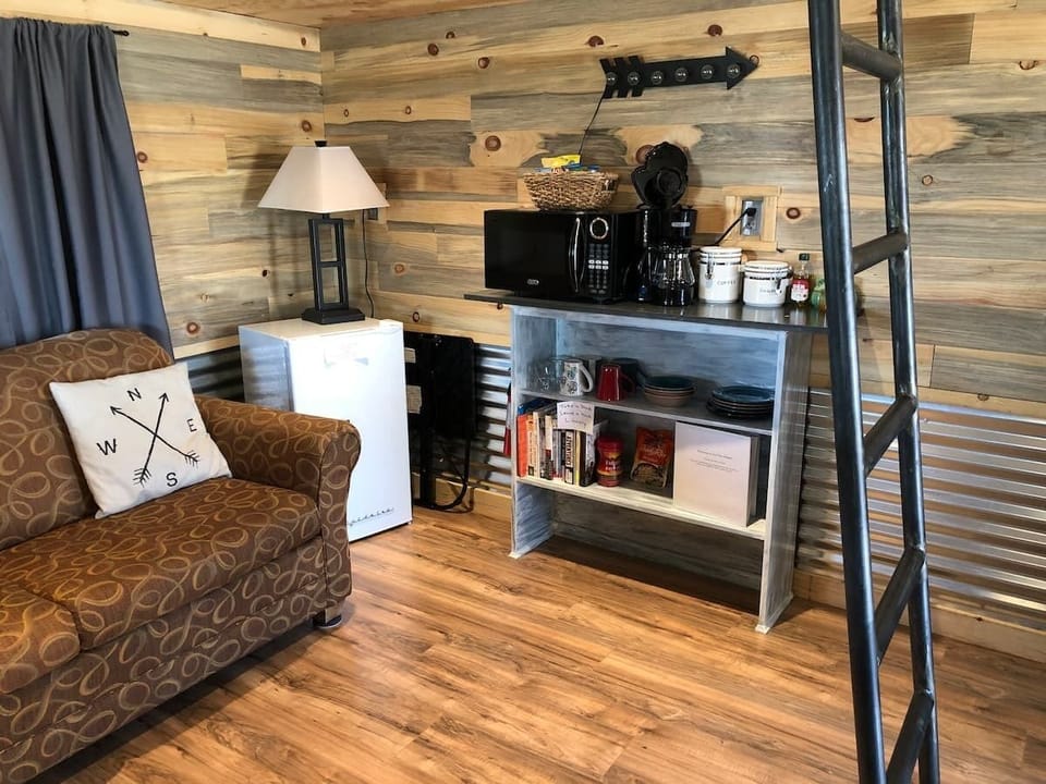 Den features a small couch, tv, mini fridge, and coffee bar