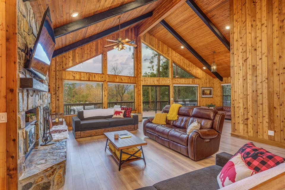 Mountain style open concept, High ceiling living room with a  stone fireplace. Summit Cabin radiates rustic charm!
