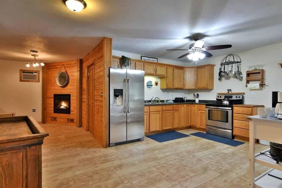 A kitchen view in the Highland Cottage featuring oak cabinets, a stainless steel stove with a tea kettle, a white kitchen island with a coffee station, and a dark countertop.
