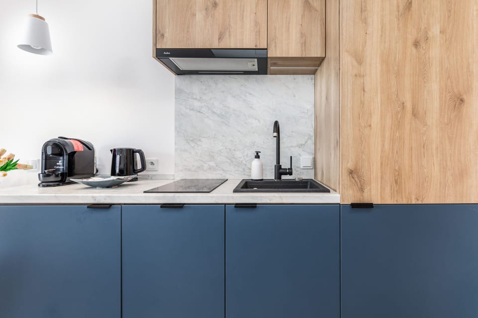 A modern kitchen with wooden cabinets, navy blue finishes, and sleek black appliances.
