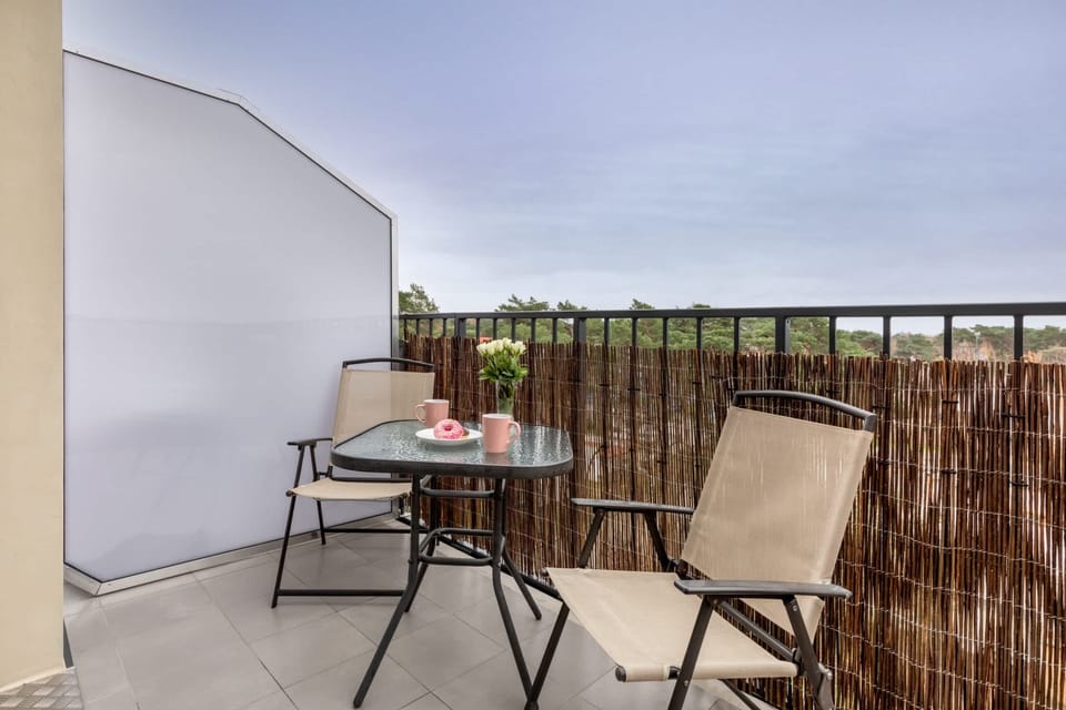 A balcony with a table and two chairs, overlooking the lush green landscape. Perfect for outdoor relaxation with privacy fencing.