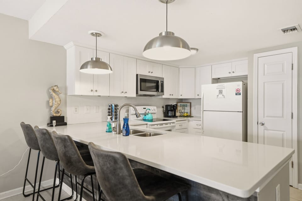 Cook with ease in the fully equipped kitchen featuring bright white cabinetry, ample counter space, and bar seating.