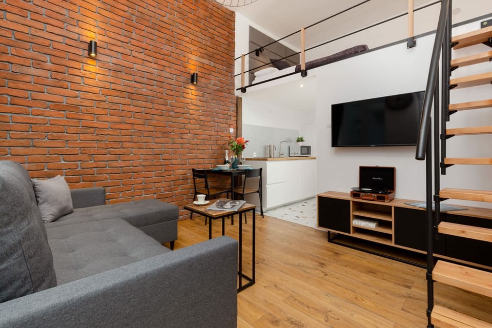 Another view of the living room, featuring a comfortable sofa, industrial lighting, and natural brick walls.
