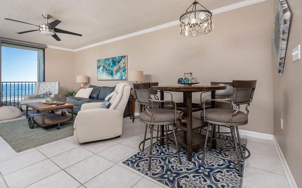 The living area features a blue sofa with a queen sleeper, stylish chairs, and a dining table with bar stools on the gulf
