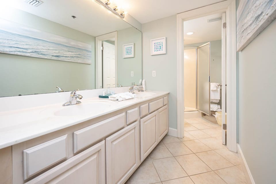 Master bathroom featuring dual sinks, a walk-in shower, and beach-themed artwork for a refreshing vacation experience