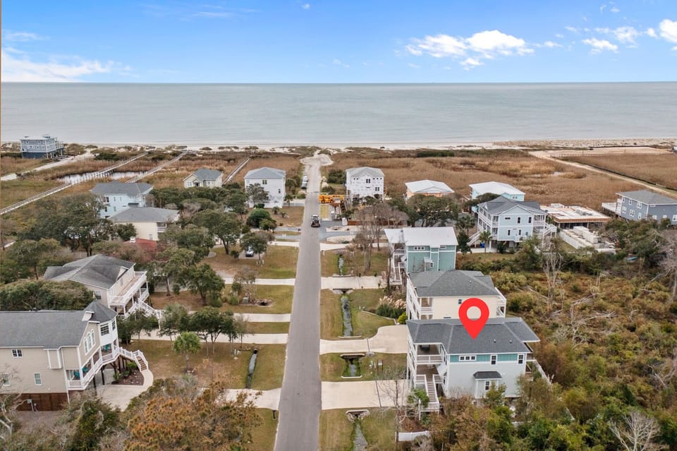 Aerial view of quiet Oak Island beachside neighborhood with coastal homes, street leading directly to the ocean, marsh areas, and the highlighted vacation rental location near the beach.