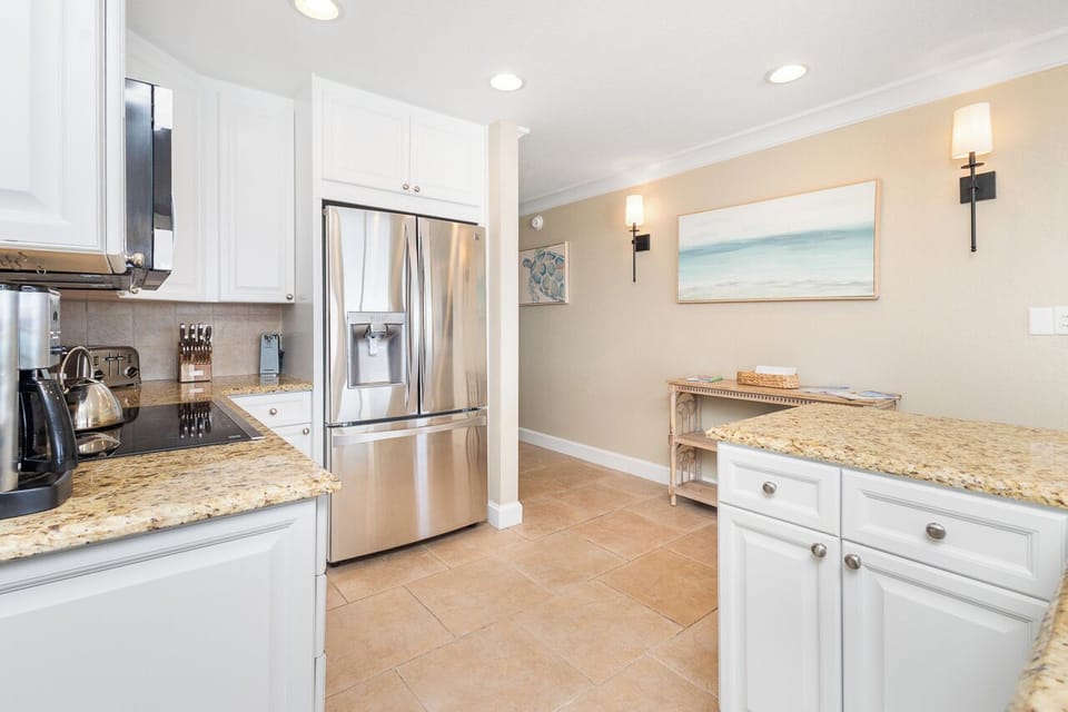 Your fully equipped kitchen features granite counters, stainless appliances, and coastal artwork—perfect for preparing memorable meals during your stay.