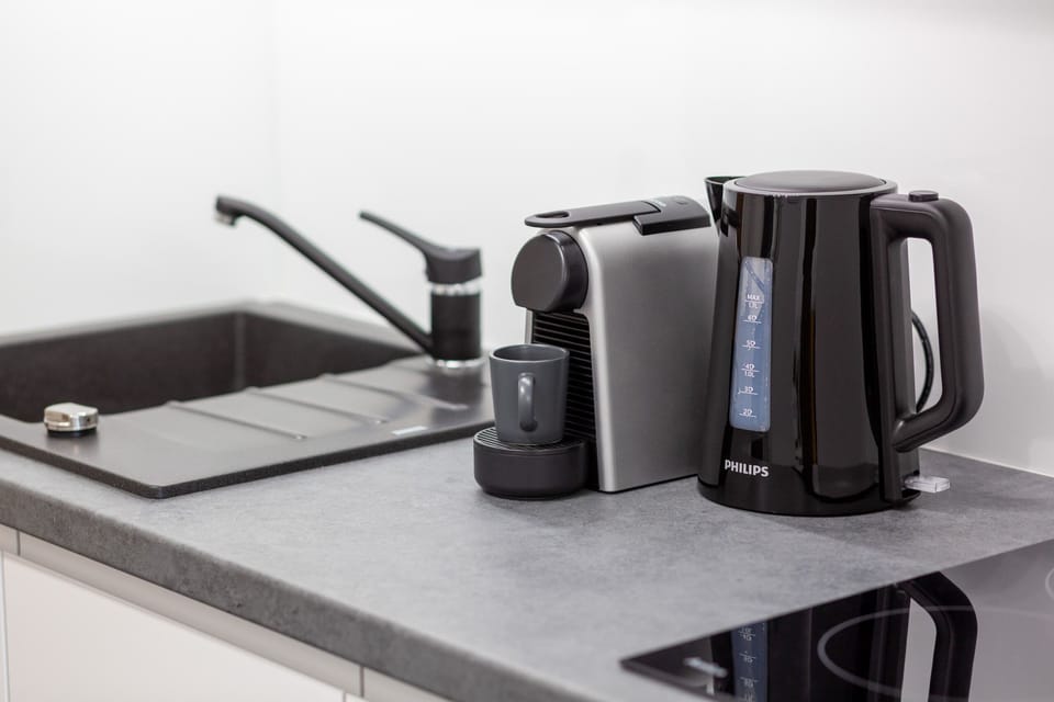 A black countertop with a coffee maker and kettle, blending practicality and contemporary design.
