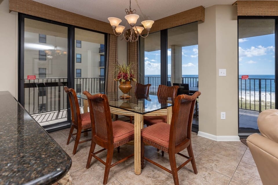 Dining area features a glass-top table with chairs, offering a view of the gulf through expansive windows