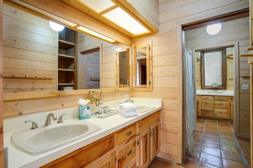 Bright skylights illuminate warm wood walls and double vanity sinks, creating a welcoming space for your morning routine with fresh towels and thoughtful amenities.