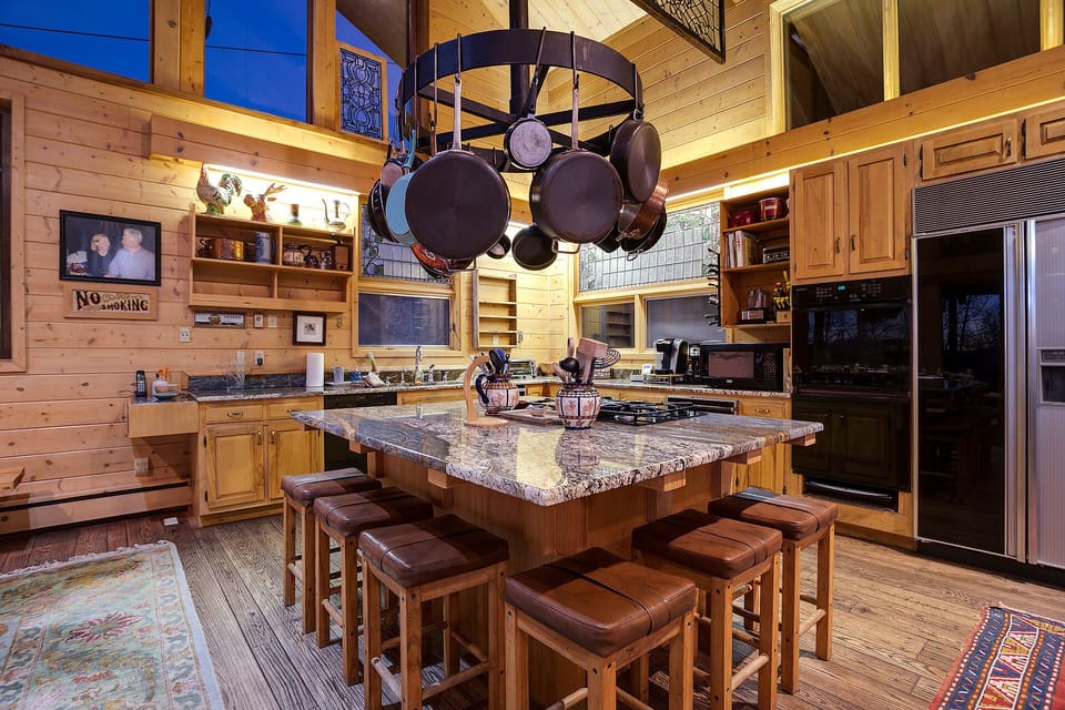 Gather around your granite island with hanging pot rack, where culinary adventures await in this warmly lit, rustic kitchen sanctuary.
