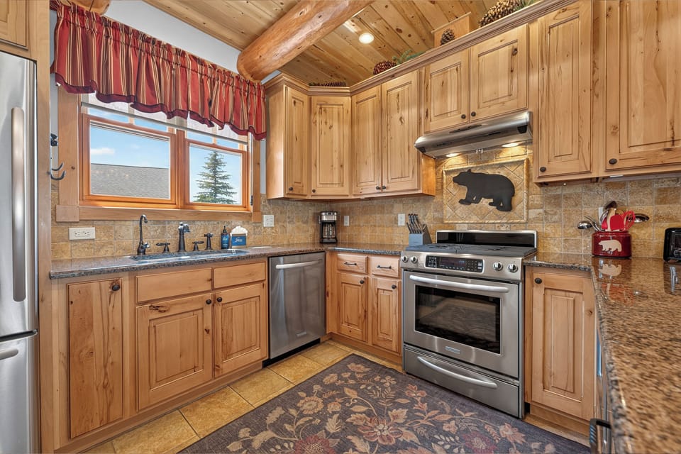Your mountain retreat includes a fully equipped kitchen with rich knotted pine cabinetry, granite counters, and stainless steel appliances—perfect for preparing hearty meals after a day of adventure.