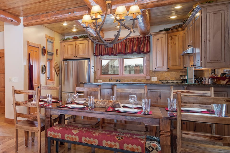 You'll love gathering around this rustic dining table under the antler chandelier, creating memories in this cozy mountain-style kitchen and dining space.